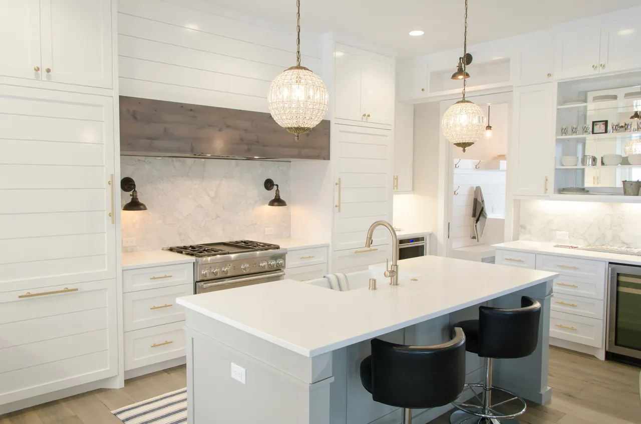 White kitchen with a large island, pendant lights, brass hardware and pale wood flooring