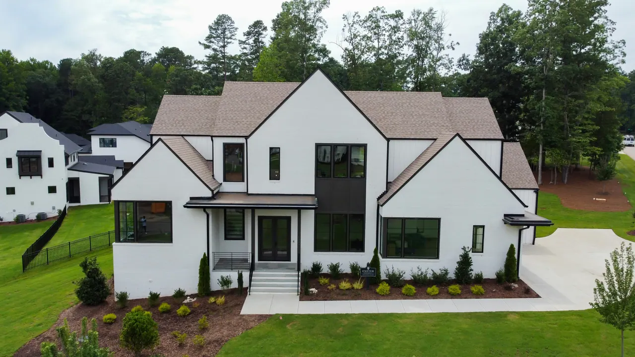 White detached home with gabled roofs, black-framed windows and a landscaped front lawn