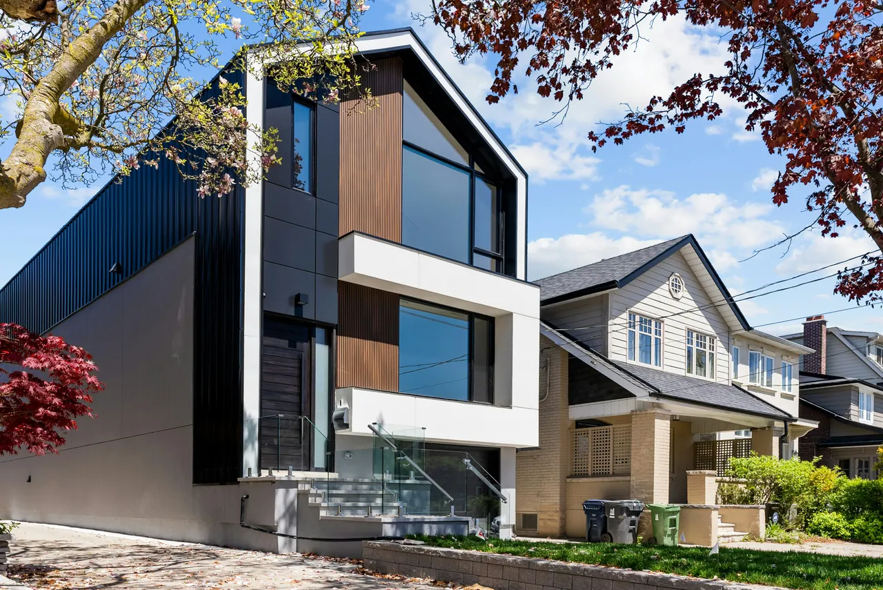 Contemporary narrow-lot home with dark cladding, wood accents, tall windows and glass-railed front steps